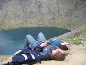 Dan and Claire lounge on a rock above a lake.