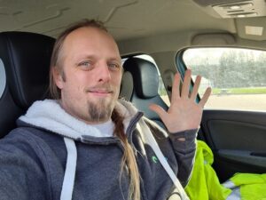 Dan waving, sat in a car.