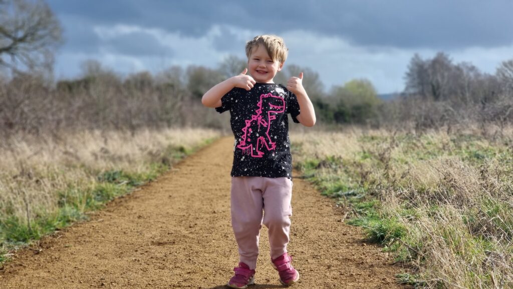 Five year old boy on a footpath with two thumbs up.