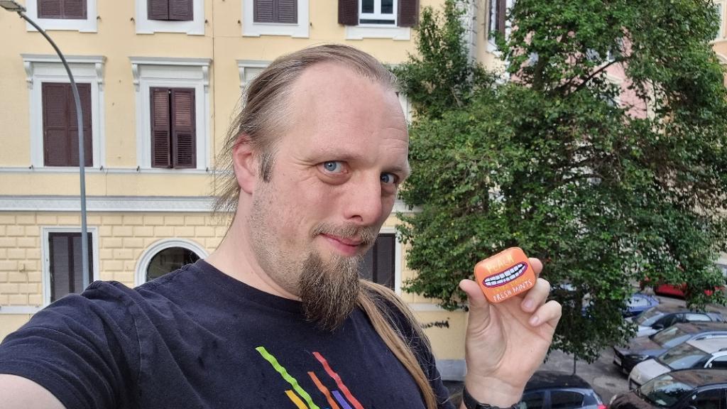 Dan holding an orange mint tin in a city centre.
