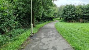 A concrete path running between mowed grass past a lamp post.
