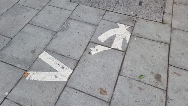 Photograph of paving slabs: a glyph of a walking person, signifying "walk here", has been painted onto the flagstones, but the stones have since been lifted and replaced in slightly different locations, making the person appear "scrambled".