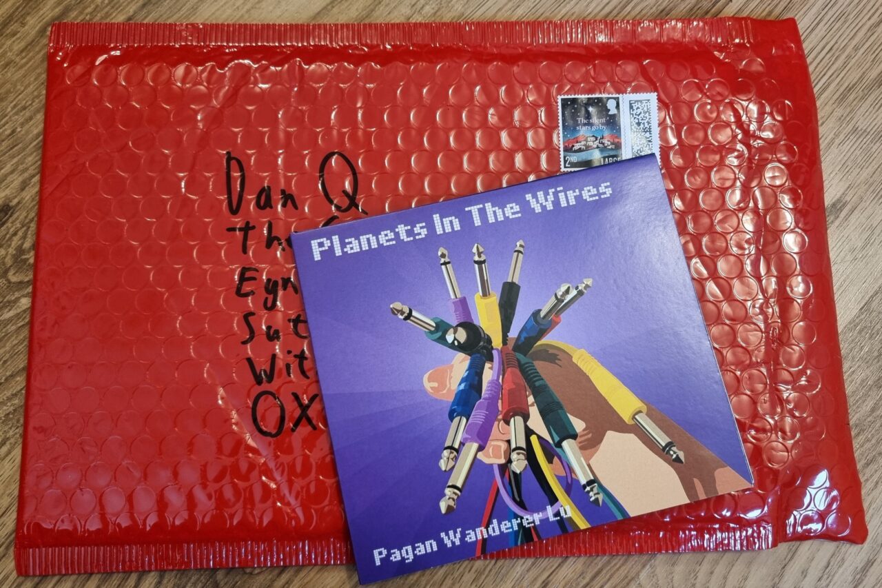 Slim CD case of the album atop a padded envelope made of red bubble wrap.