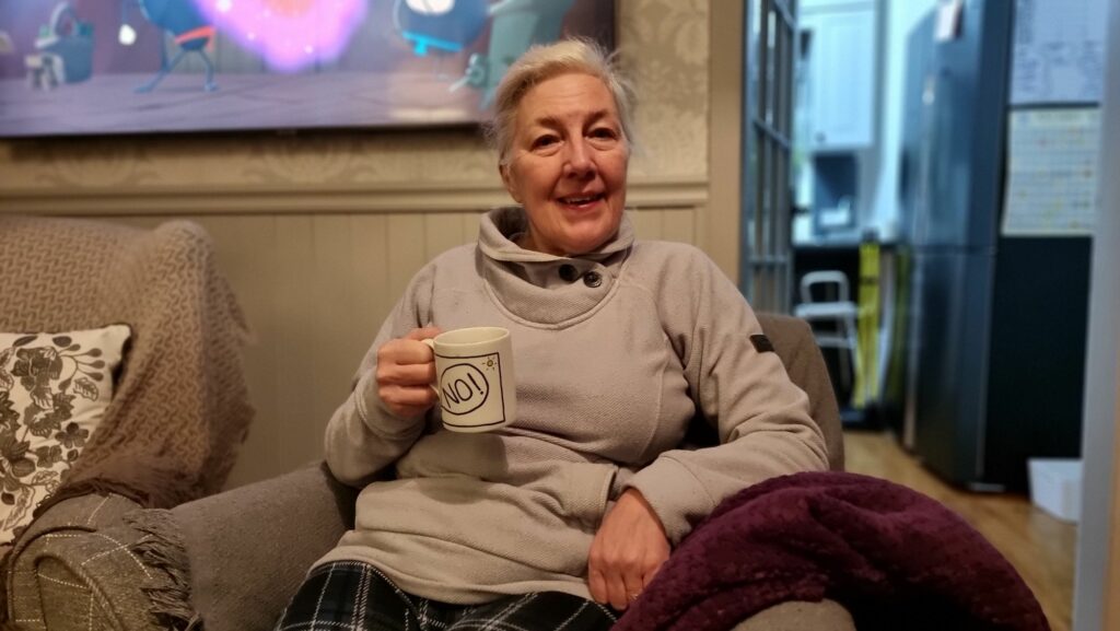 A white-haired woman sitting on a comfortable chair holding a mug.