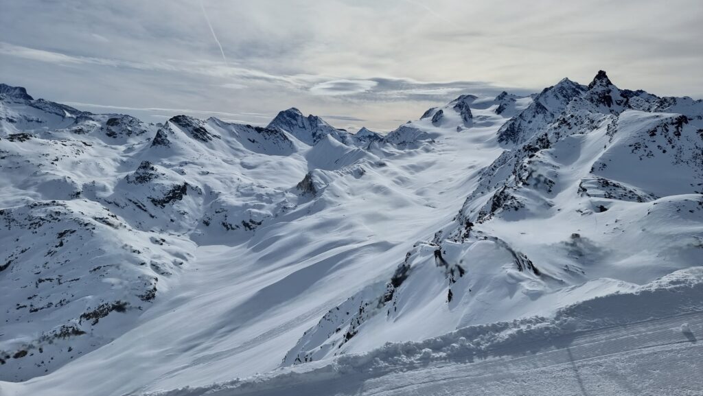 A snow-covered Alpine glacier sandwiched into a gully of exposed rocks.