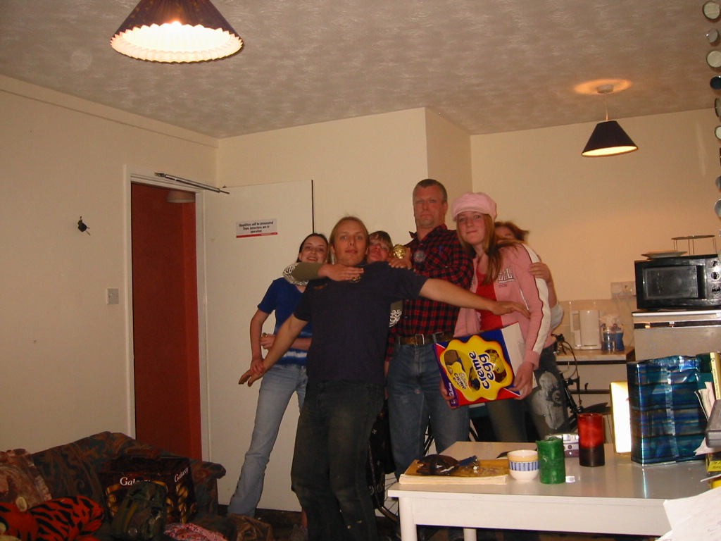 Dan, aged 22, stands in a cluttered flat with his partner Claire and several members of Dan's family.
