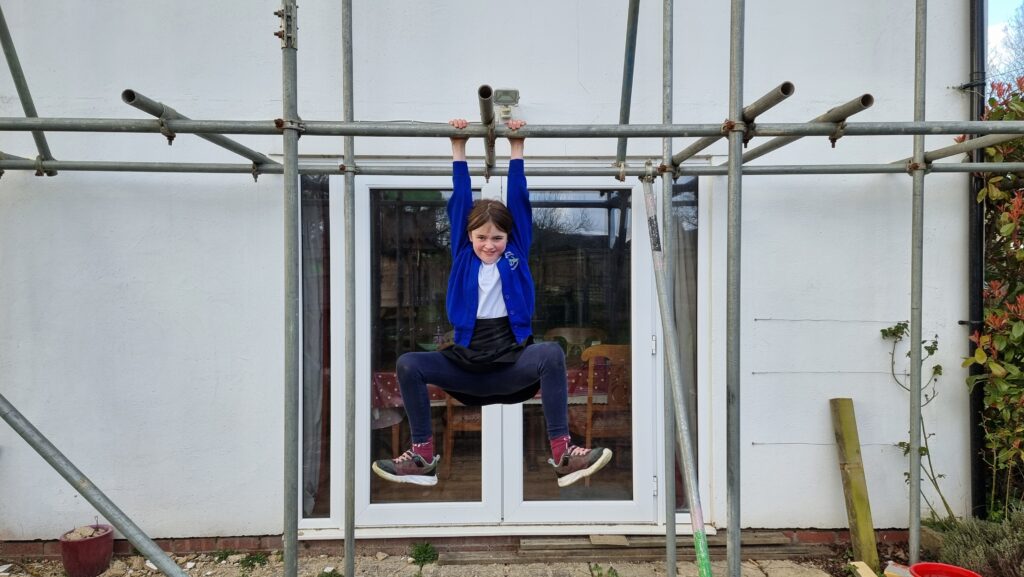 A 10-year-old girl hangs from a scaffolding pole outside a white house.