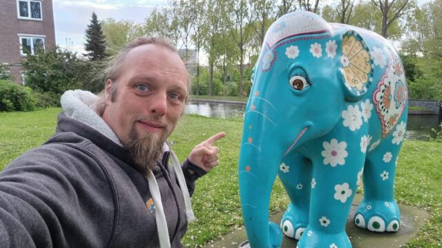 Dan crouches next to a statue of an Indian elephant painted with flowers.
