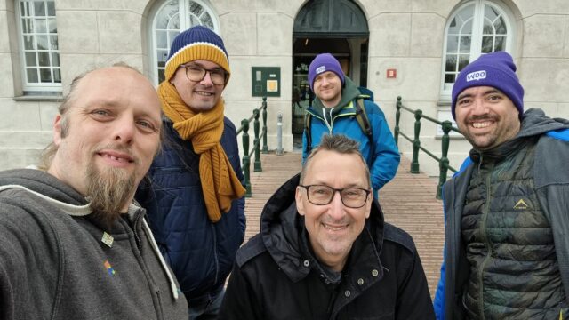 Five men in thick coats stand at the entrance to a museum.