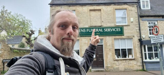 Dan points to a bricked-up first storey window on a stone building used by a funeral services company.