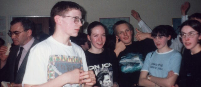 A group of teenagers stand around awkwardly.