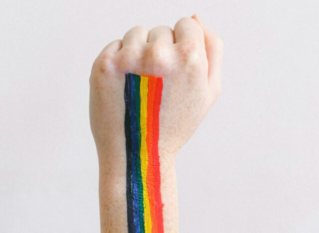 A pride rainbow painted down the back of a white person's first, held in the air.