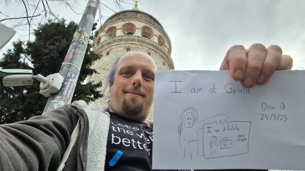 In front of the Galata Tower, Dan holds up a sign that reads 'I am at Galata' and depicts him holding up a sign that reads 'I am at Galata' and depicts him holding up a sign, and so on...