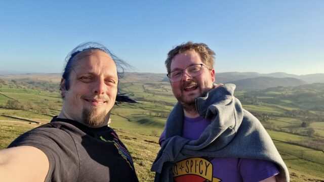 Two white men stand on a windy Lake District hilltop.