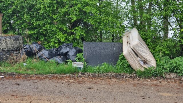 A fly-tipped mattress and bin bags in a layby.