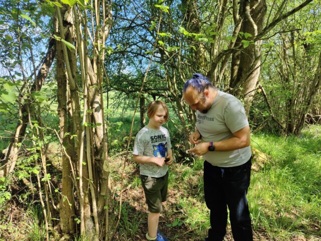 Dan helps a child open a small geocache container, in a forest.