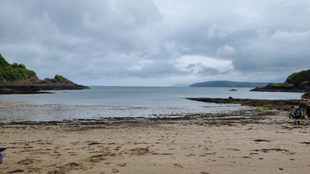 Sandy beach in front of a narrow bay, flanked by cliffs, under turbulent skies.