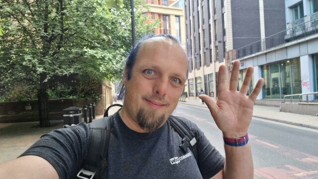 Dan waves from a leafy urban street.