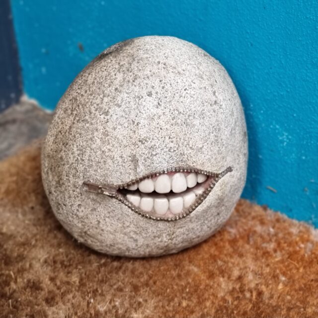 Sculpture of a rock with a zipper mouth behind which can be seen an uncannily-realistic set of teeth.