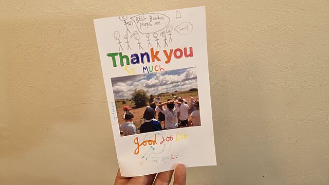 A hand-coloured card, saying 'Thank you so much', with a child's drawing of somebody talking about Bell Beaker people and a photo of Dan showing pictures of pots to a class of schoolchildren.