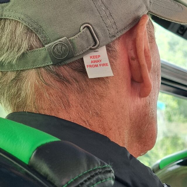 On a bus, back abs sides of a man's head. His hat has a label which reads "keep away from fire", but it's hanging out in such a way that it looks like it might be his head that's labelled.