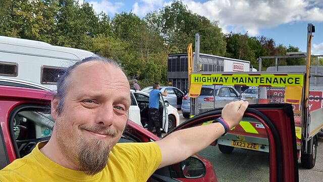 Dan stands among stationary cars and other frustrated drivers on a motorway.