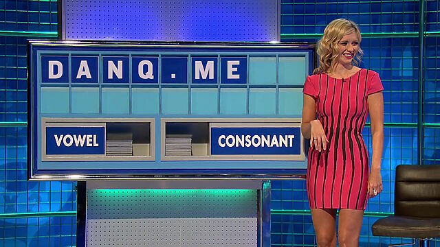Rachel Riley, wearing a pink and black dress, stands in front of a partially-filled Countdown board showing the letters 'DANQ.ME'.
