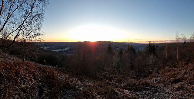 Sun rising over a hill beyond a broad valley full of frozen fields.