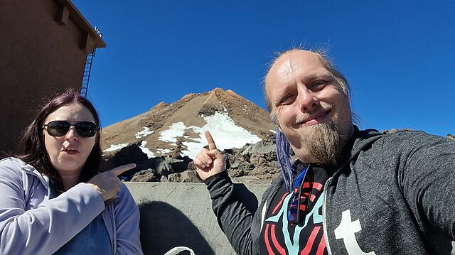 Dan and Ruth stand in front of a partially-snow-covered volcano cone.