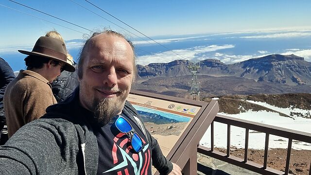 Dan stands by an information board in front of a broad volcanic crater.