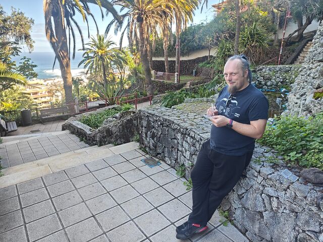 Dan leans against a wall in a tropical park, writing on a log sheet.