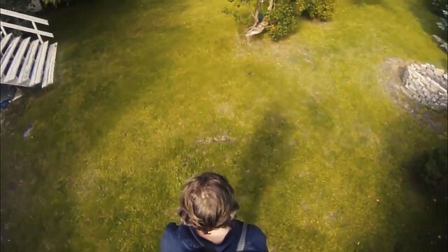 From a pole, a view looking down upon the top of the head (and the ground in front of) a man wearing a VR headset outdoors; the view is similar to that used in third-person videogames.