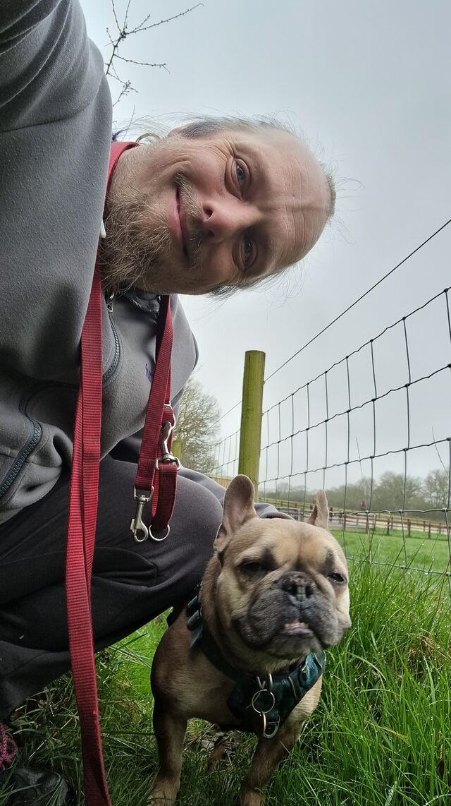 Dan crouches by his French Bulldog on a rural footpath.