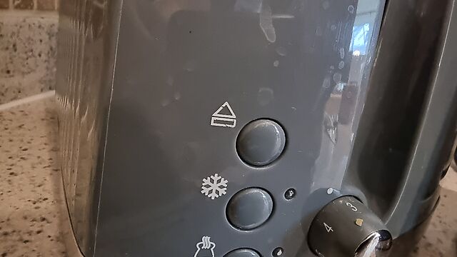 Close up of the side of a toaster, showing an "eject" button (rectangle with an upward-pointing triangle above it).