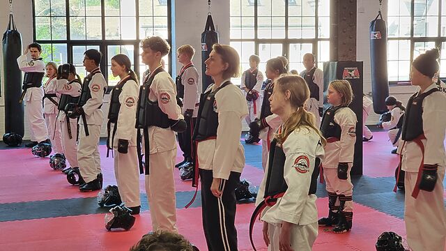 A mixed age group of people dressed in taekwondo robes with a mixture of red and black belts.