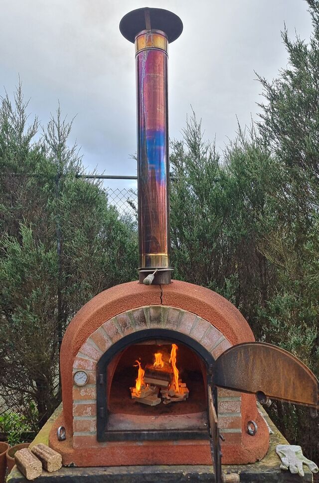 The same brick pizza oven, now seen from a few steps back with its chimney and base visible.