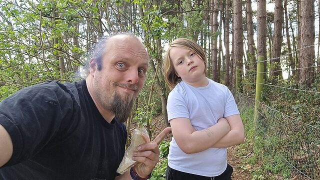 Dan and a boy holding cling-wrapped sandwiches in a forest.