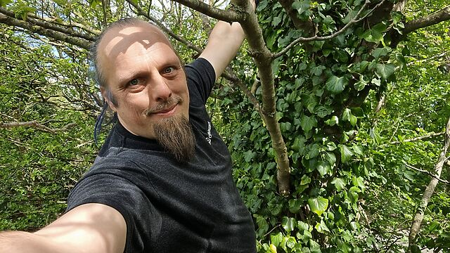 Dan hangs from a tree; a cache container is barely visible in the background.