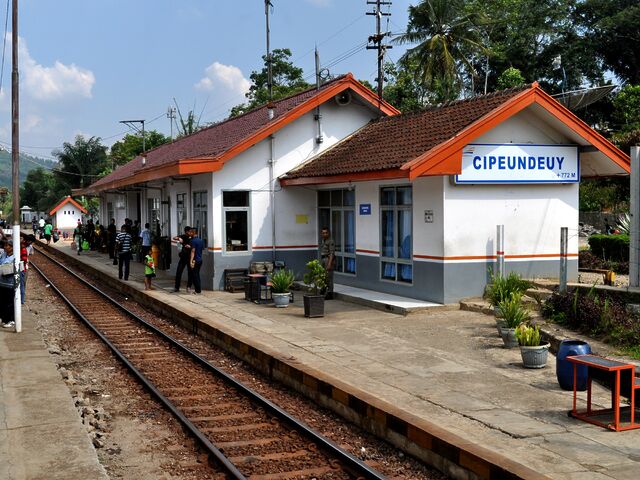 Cipeundeuy Railway Station, a small white building with a railway track running alongside, with people on the platform.