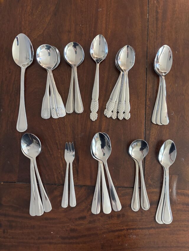 11 small piles of stainless steel flatware sorted by type, with 1-7 items per pile. 10 types are spoons, 1 is tiny forks.