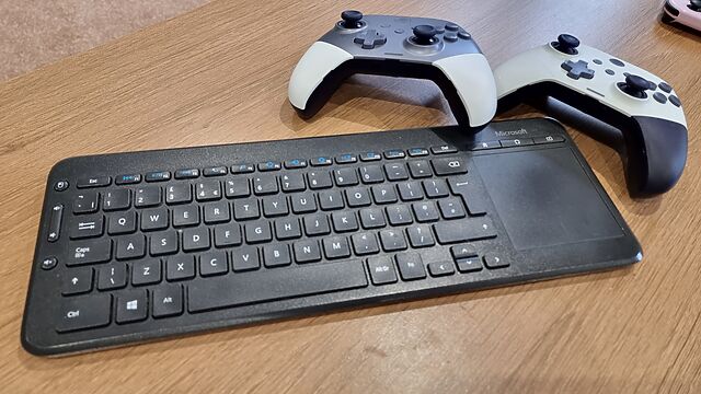 A slim Microsoft all-in-one keyboard and touchpad, in British layout, alongside two game controllers.
