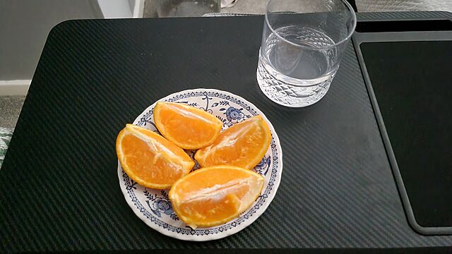 An orange, sliced into quarters, alongside a glass of slightly-opaque water.