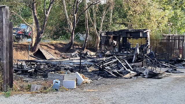 A handful of metal frame struts stick out from an ash pile that was clearly once a static caravan.