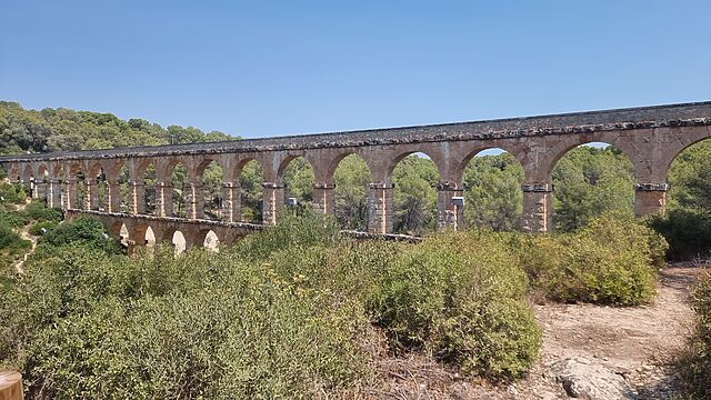 A Roman aquaduct spans a forested valley.