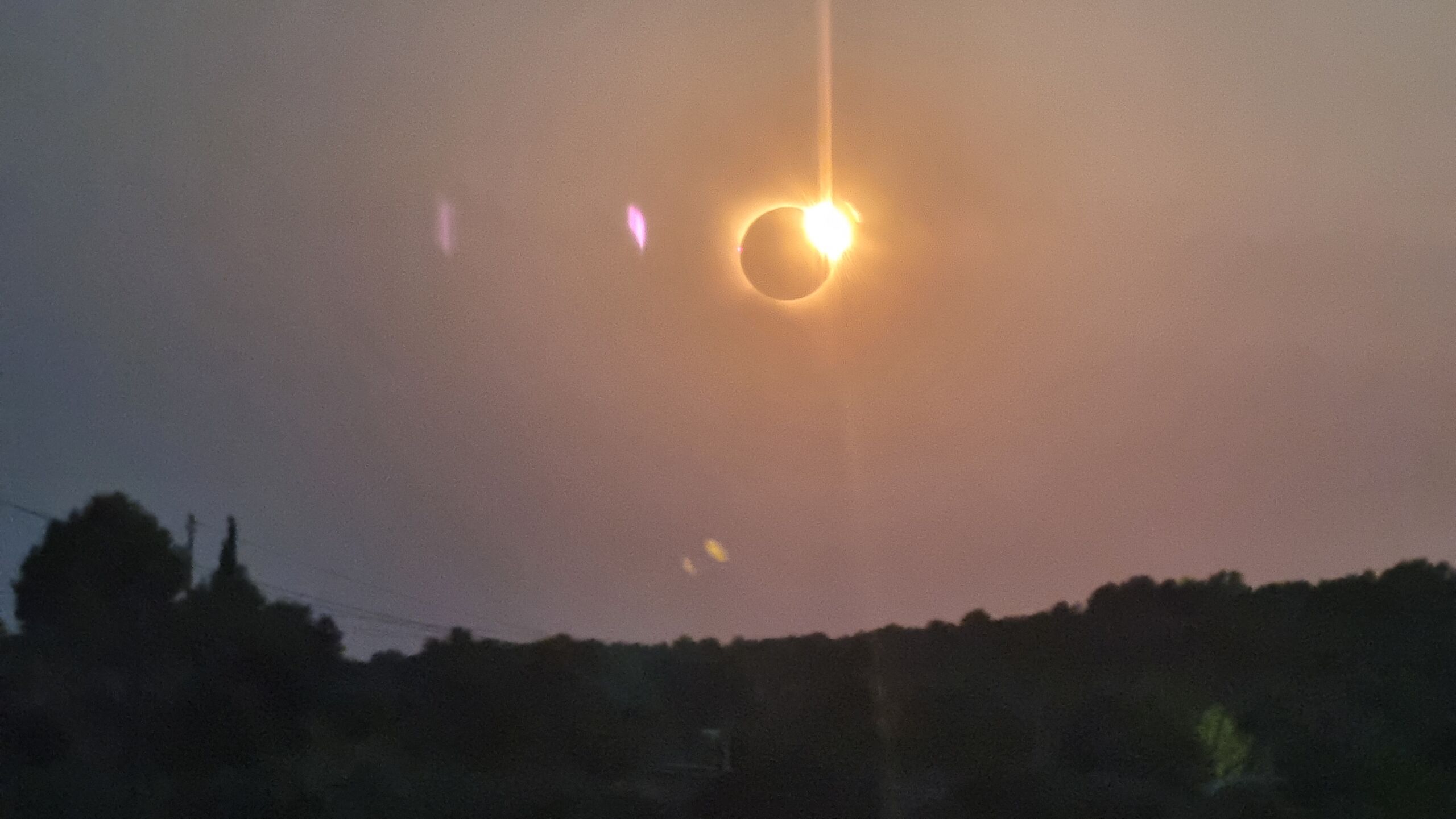 Over the silhouette of hills, a total solar eclipse is just coming to an end, with a 'diamond ring' effect resulting from the sun's reappearance visible.