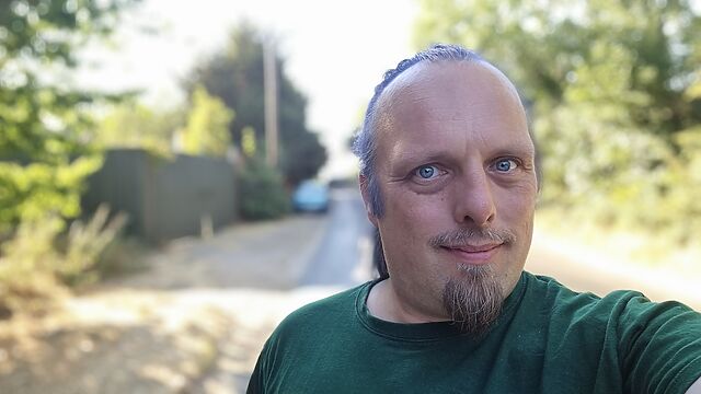 Dan walks down a country lane, a parked car in the background.