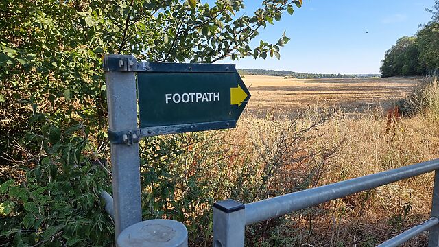 A footpath sign alongside a recently-cut field.