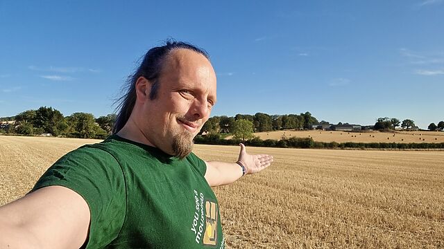 Standing in a field, Dan raises his arms in victory.