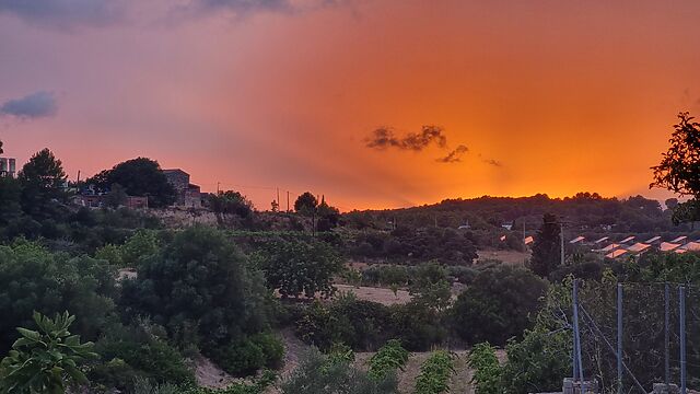 A red and orange sunset with beams reaching up over the hilly horizon of climatically- Mediterranean farmlands.