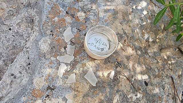 A bottle top style lid, with Dan's name written in it, sits alongside some plastic shards on top of a rock.